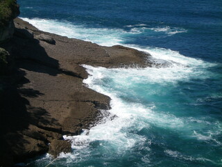 Olas del océano chocando contra las rocas de un acantilado en una playa.