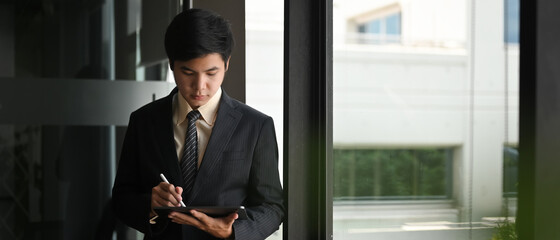 A businessman is using a computer tablet and stylus pen while standing in the modern office.