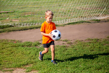 little soccer player walks across the field with the ball in his hands