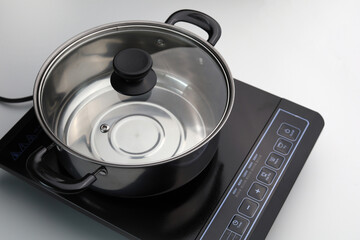 Modern stainless steel cooking pot with a transparent glass lid on an induction stove.