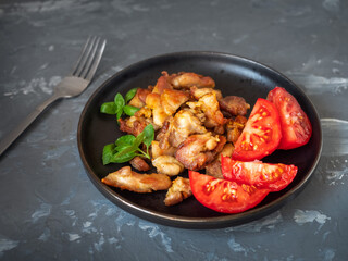 Breakfast with chicken fried fillets and chopped red tomatoes on a round dark plate and basil leaves