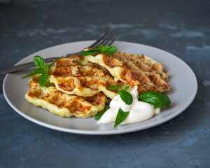 Zucchini shoes with the addition of cheese on a light plate top viewZucchini waffles with sour cream-mushroom sauce and basil leaves on a light plate with a table fork for