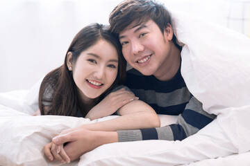 Happy Asian couple teasing each other on the bed in the bedroom.