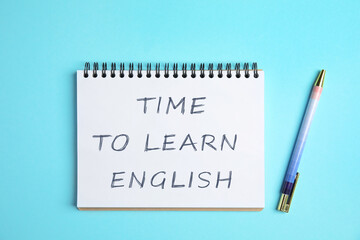 Notebook with text Time To Learn English and pen on light blue background, top view