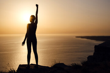 silhouette of woman with raised hands on the beach at sunset
