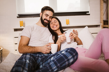 Obraz na płótnie Canvas Young happy couple drinking coffee in bed at morning
