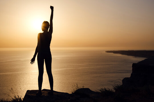 Silhouette Of Woman With Raised Hands On The Beach At Sunset