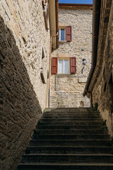 Fototapeta na wymiar An old staircase in a narrow passage between the walls. Windows on the facade. Italy