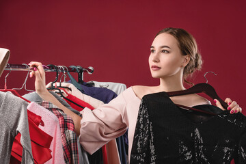 Fototapeta na wymiar Beautiful women chooses and tries on clothes on a red background. The concept of choosing and buying clothes, shopaholism and consumerism