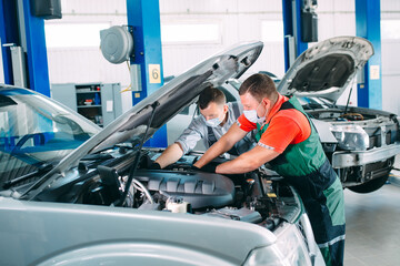 A masked mechanic checks the car at the service station.