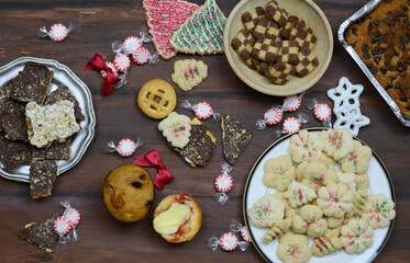 Flat lay of a varitey of sweets and goodies witha Christmas theme on a rustic wooden tabletop. Includes homemade candies and cakes and cookies