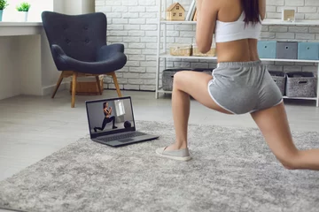 Gordijnen Online fitness at home. The girl does exercises watching the video course the trainer has a laptop at home. © Studio Romantic