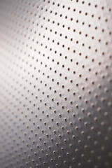 Perforated aluminum surface with many holes. Their ranks go into the distance and form a perspective. Dark vertical wallpaper. Industrial gray metal background. Macro