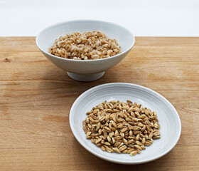 Boiled spelt in a bowl isolated on wooden background with seeds