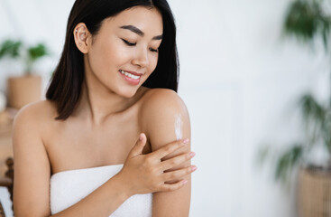 Obraz na płótnie Canvas Smiling asian girl applying body lotion on her shoulder