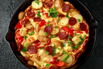 Frittata made of eggs, potato, chorizo, red bell pepper and greens in iron cast pan