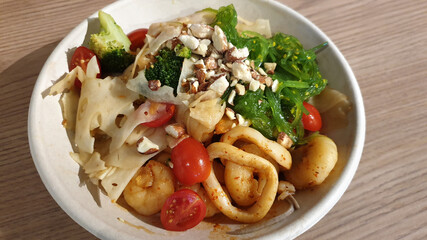 Salad with squid, onion, tofu, cherry tomato, slice lotus roots, seaweeds salad and nuts on wooden table