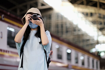 Fototapeta premium Asian travelers girl take a picture in train station with medical face mask to protection the Covid-19, new normal lifestyle