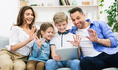 Family Making Video Call On Tablet Waving Hello At Home