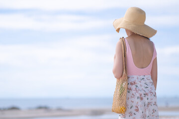 Asian girl with pink bodysuit and straw hat on the beach
