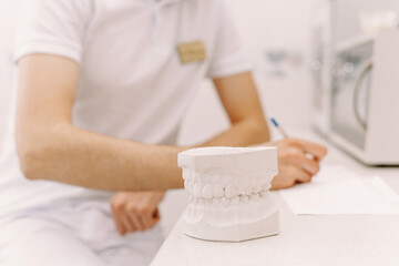 The concept of writing to the dentist. The man writes something on the patient's medical record. In the foreground is an artificial jaw