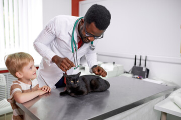 handsome african doctor veterinarian is examining cute cat while his owner is standing nearby, confident doctor inspires confidence