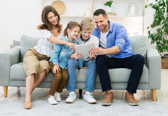 Happy Family Using Tablet Computer Together On Couch At Home