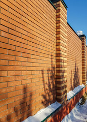 Modern red brick fence with turrets, in winter, outdoors © clairelucia