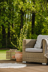 Wicker armchair with pillow on green terrace in beautiful garden