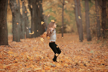 Beautiful smiling girl throws autumn leaves in the park. Warm happy family day in the wood