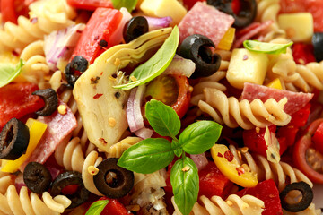 Antipasto salad with pasta, tomato, olives, red onion, bell pepper, salami, cheese, artichoke and basil.