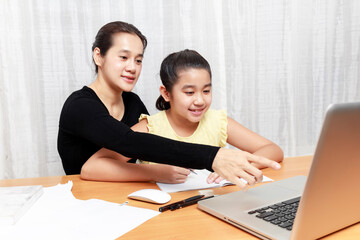 Asian young little girl using pencil to do homework with her mother. Student kid writing  homework book. Girl use computer to study at home. Education homeschool  concept.