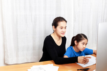 Asian young little girl using pencil to do homework with her mother. Student kid writing  homework book. Girl use computer to study at home. Education homeschool  concept.