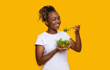 Healthy african woman eating fresh salad over yellow
