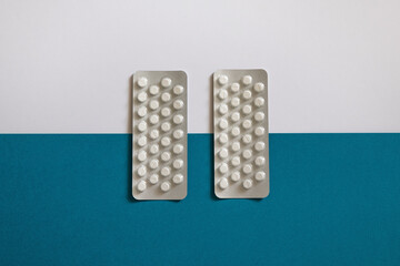 Two strips of oral contraceptive pills laying flat against blue and white background, women's hormonal birth control medication, concept for feminine health, gynecological issues or planned pregnancy