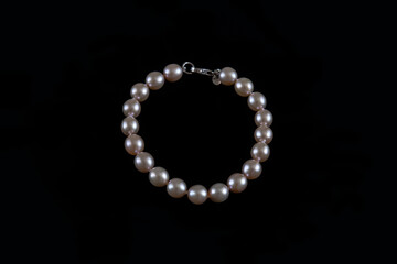 Genuine round pearls bracelet in ivory color against a black background, elegant precious organic jewelry worn as accessory for a formal or a casual-chic attire or as birthstone for the month of June