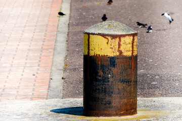 Rusty bollard with yellow paint at the top on the concrete floor of the pier in the harbour