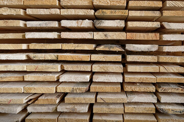 Stack of natural rough wooden boards close-up. Storage of wood in a carpenter's workshop or at a sawmill