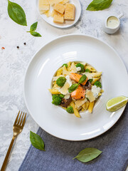 Pasta penne with salmon, broccoli, and pesto sauce on the white-gray background. Flat lay.