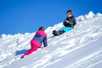 Two joyful kids playing on the snowing mountain on a winter day. Brother and sister