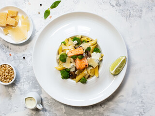 Pasta penne with salmon, broccoli, and pesto sauce on the white-gray background. Flat lay.