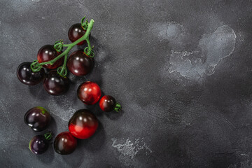 Indigo Rose heirloom cherry tomatoes on the vine atop washed dark concrete backdrop, top view