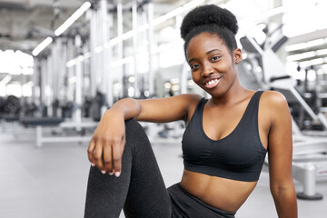 Fototapeta na wymiar portrait of adorable african lady sitting in gym, young lady in sportswear after crossfit exercises, posing, smile. healthy lifestyle concept