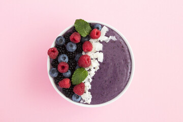 Top view of smoothies bowl with berries  and coconut chips on the pink surface