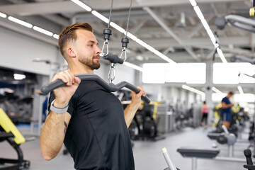 young caucasian man trains on fitness equipment in the gym, pumps arms muscles, healthy lifestyle