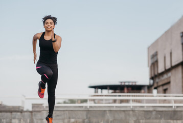 Morning run and workout. Happy african american girl in sportswear and sneakers, with fitness tracker runs