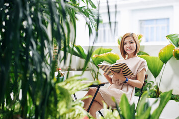 Obraz premium Portrait of attractive smiling young Asian woman enjoying reading book in cafe