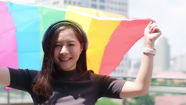 Happy loving homosexual lesbian LGBT couple with rainbow flag at city streets at sunset. Portrait of happy lesbian LGBT woman wraped herself in rainbow flag. slow motion.