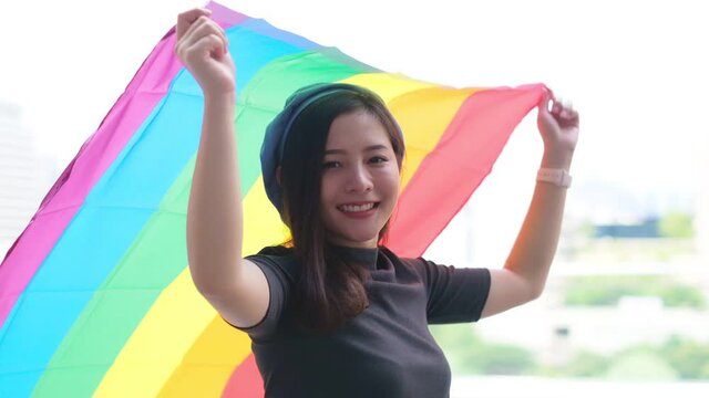 Happy loving homosexual lesbian LGBT couple with rainbow flag at city streets at sunset. Portrait of happy lesbian LGBT woman wraped herself in rainbow flag. slow motion.