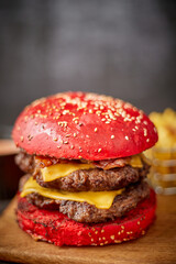 Homemade red sesame bun double bacon cheese burger. Served with french fries on wooden board.